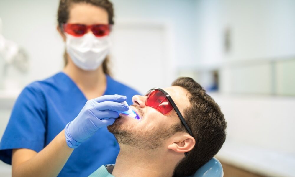 Dentist using laser device for teeth treatment on patient wearing protective glasses.