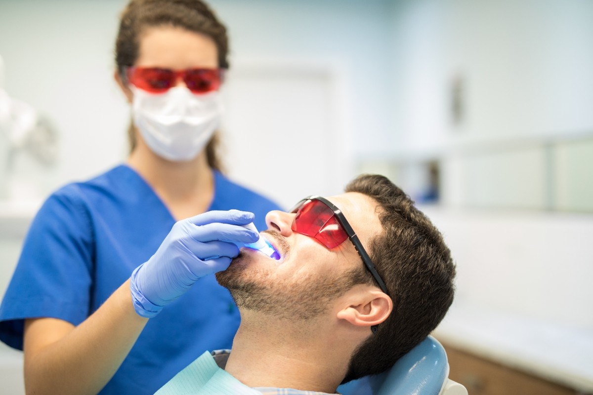 Dentist performing laser dental treatment on man in modern dental clinic.